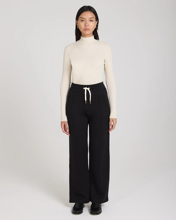 Model wearing Emello black wide-leg lyocell trousers with pin-tuck detailing and drawcord waistband.