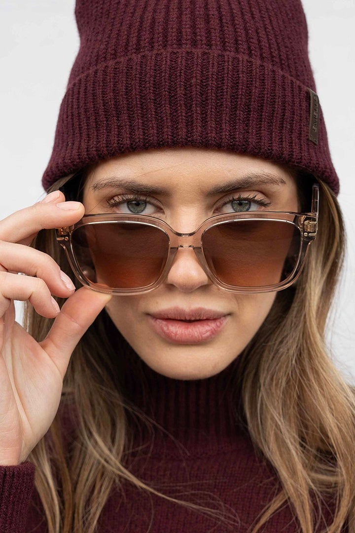 Person wearing a maroon beanie and sunglasses against a plain background