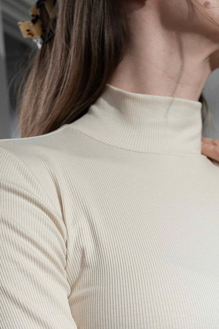 Woman wearing a beige high-neck top in a mirror reflection setting