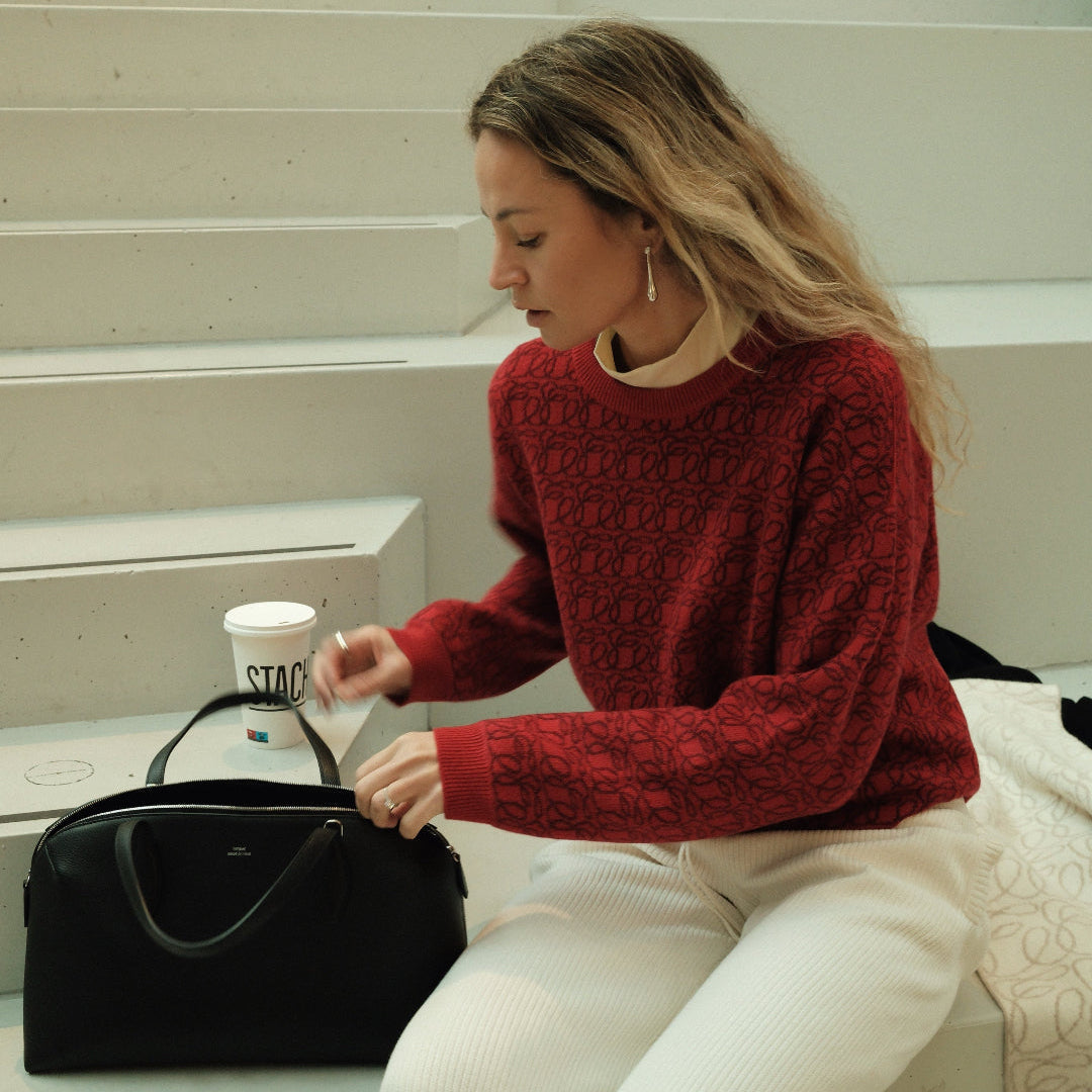 Woman in a red sweater sitting on steps with a black handbag and a white cup.