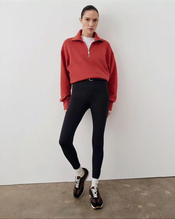 Person wearing a red sweater, black leggings, and black shoes against a white wall.