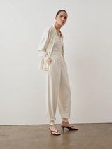 Model wearing Emello Balloon Popper Trousers in cream with relaxed silhouette and adjustable hem poppers.