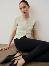 A model wearing a pale green bouclé short sleeve cardigan, seated in a composed and elegant manner.