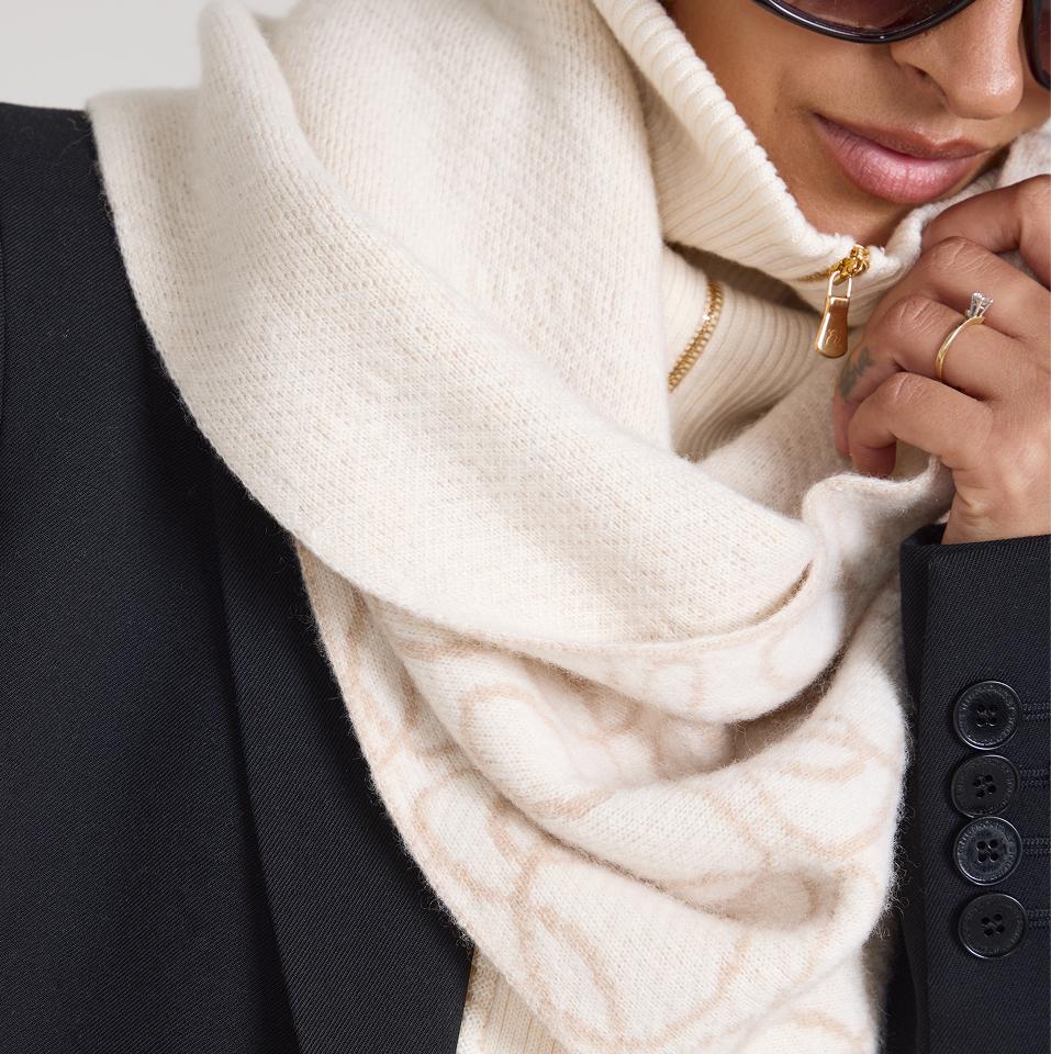Close-up of brushed cashmere scarf in soft cream, layered over a ribbed zip-up knit and tailored black coat.