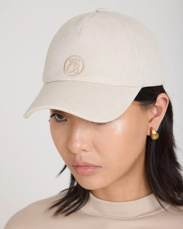 Emello Cap in beige brushed cotton twill, featuring a pale gold disc emblem, styled on a model.