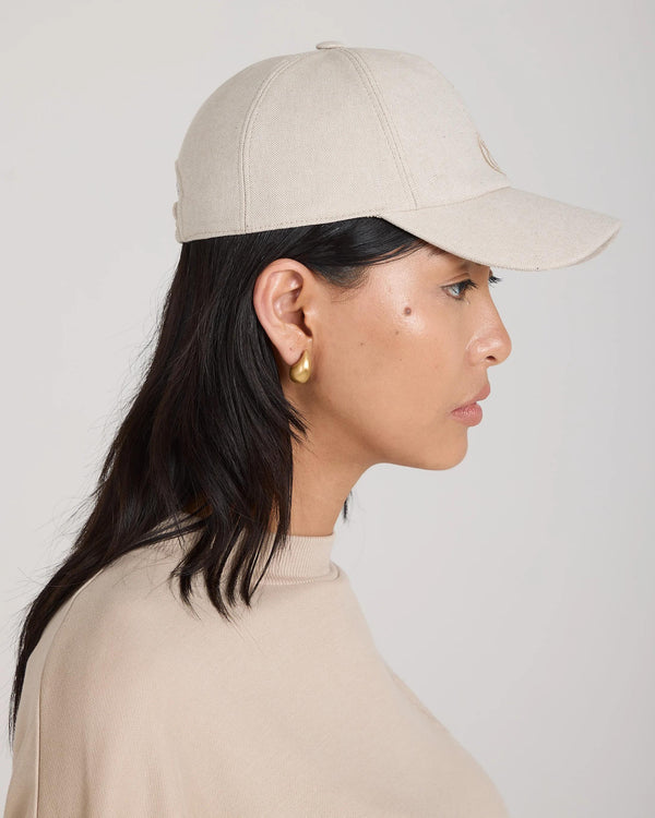 Profile view of a woman wearing the Emello beige cap, crafted in brushed cotton twill.