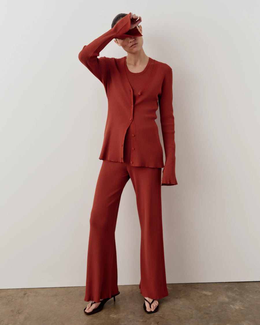 Rust red ribbed cardigan with fluted sleeves and button front, styled with matching trousers.