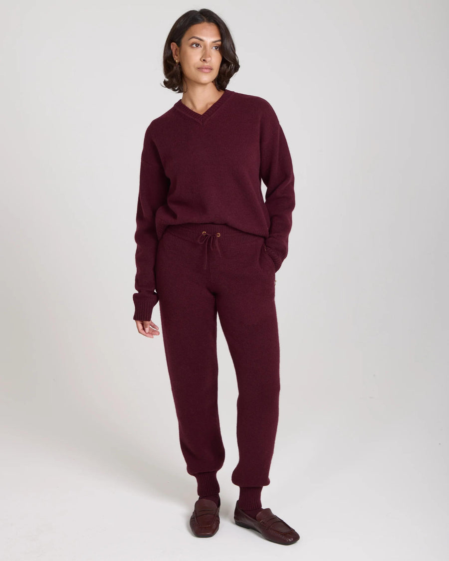 Elegant woman wearing Emello Kasima cashmere blend knit trousers in rich fig, showcasing a relaxed and refined look with gold-finish embellishments.