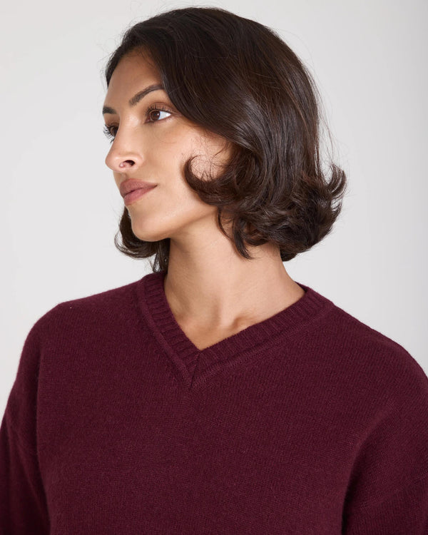 Model in a burgundy cashmere blend v-neck sweater, featuring a softly ribbed texture and relaxed silhouette.