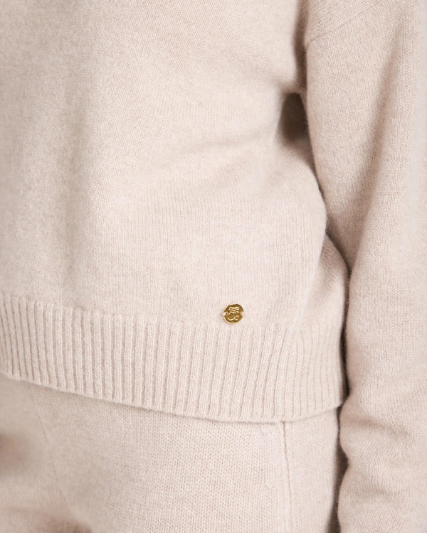 Close-up of the Kasima Cashmere Blend V Neck Sweater in beige with gold branded disc embellishment.