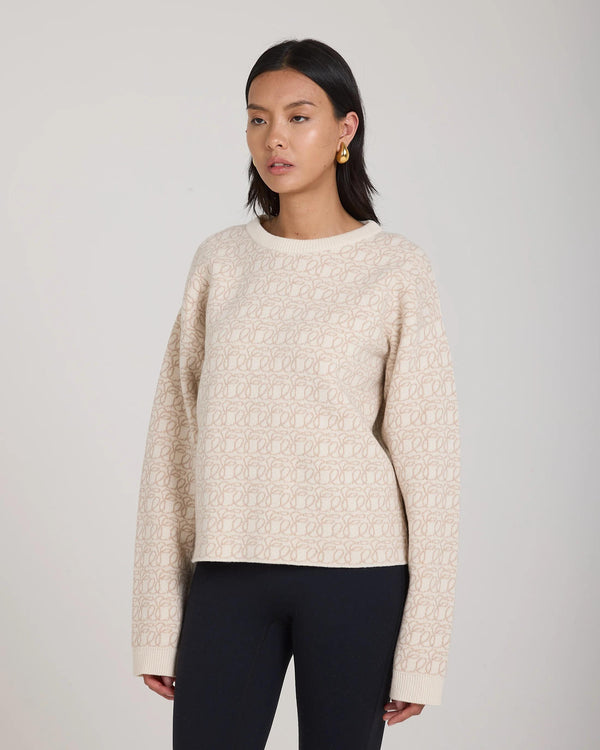 Emello's reversible jacquard cashmere sweater in cream, elegantly draped on a model against a soft daylight background.