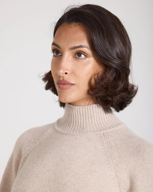 Model wearing Emello Kasima Cashmere Blend Knit Sweater in beige; featuring a relaxed fit with a rib funnel neck.