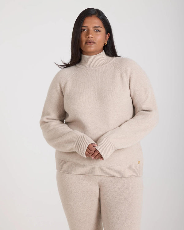 Kasima Cashmere Blend Knit Sweater in oatmeal beige, featuring a relaxed fit on a model with folded over rib funnel neck and raglan sleeves.