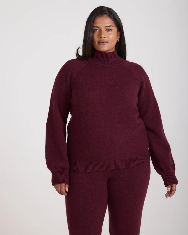 Kasima Cashmere Blend Knit Sweater in rich burgundy fig with a folded rib funnel neck, worn by a model in a relaxed pose.
