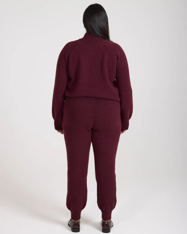 Back view of model wearing Emello Kasima Cashmere Blend Knit Trousers in Fig, showcasing ribbed cuffs and relaxed fit craftsmanship.