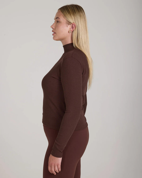 Side profile of a model wearing Emello's chocolate ribbed lyocell-cotton turtleneck top with sculptural high collar.