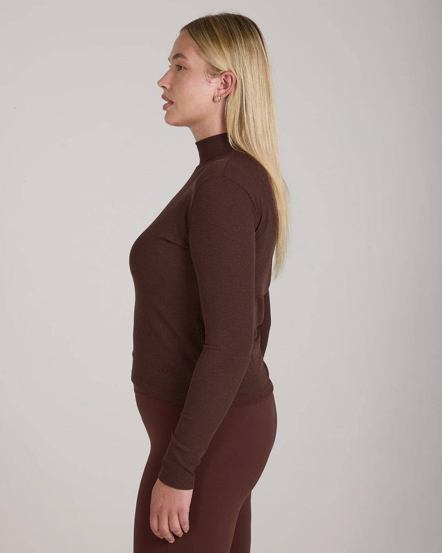 Side profile of a model wearing Emello's chocolate ribbed lyocell-cotton turtleneck top with sculptural high collar.