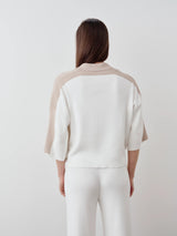 Back view of a woman wearing a white and beige contrast collar knit polo top made from organic cotton.