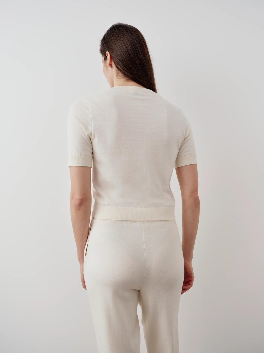 Back view of a model wearing the Emello Cotton Cashmere Knit Tee in cream, showcasing the smooth, fluid drape and ribbed trim.