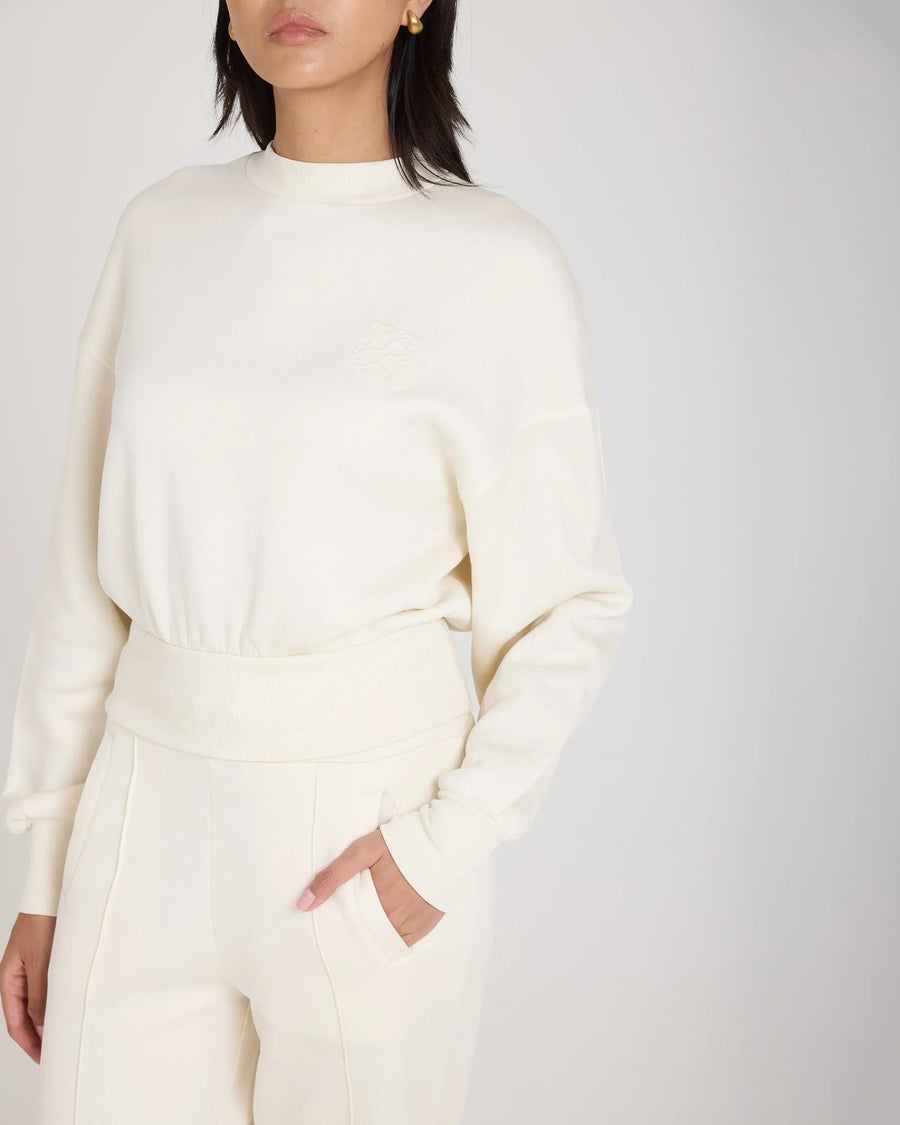 Cream sweatshirt featuring debossed logo detail, crafted from sustainable lyocell fleece with relaxed fit and pin-tuck sleeves.