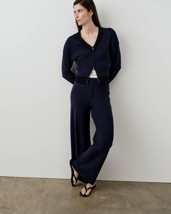 Model wearing navy Double Waistband Knitted Trousers and matching V-neck cardigan, standing against a minimalist neutral background.