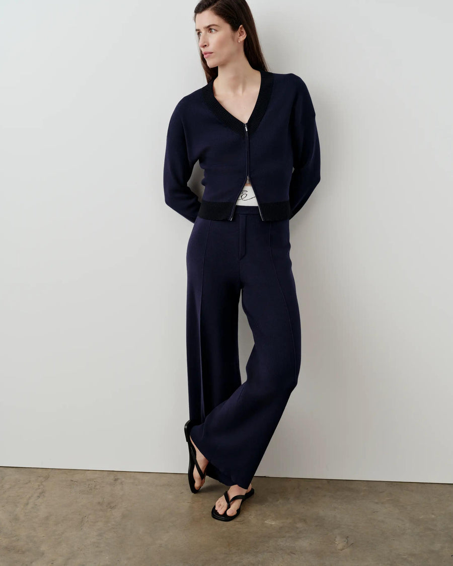 Model wearing navy Double Waistband Knitted Trousers and matching V-neck cardigan, standing against a minimalist neutral background.
