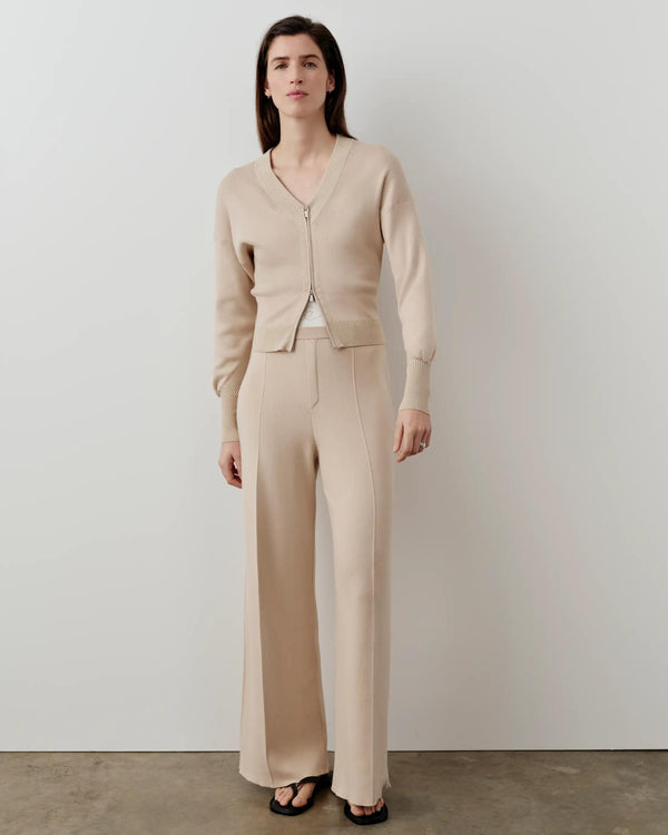 Luxury double waistband knitted trousers in a neutral tone, worn by a model pairing with a matching V-neck cardigan.