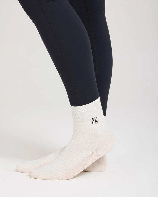 Cream ribbed half-crew socks with black embroidery worn on model, showcasing refined elegance and artisanal luxury.