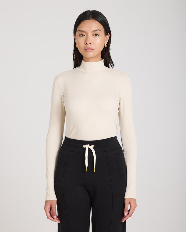 Emello Forma Ribbed Lyocell-Cotton Blend Turtleneck Top in Beige, worn by model.