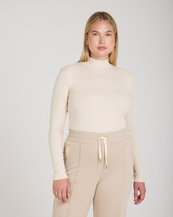 Beige ribbed turtleneck in a slim fit, crafted from lyocell-cotton blend, worn by a model with long blonde hair.