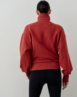 Back view of model wearing a rust red Emello half-zip funnel-neck sweatshirt with blouson sleeves.