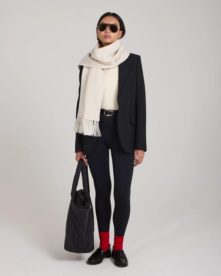 Model wearing a cream jacquard cashmere scarf with fringed tassels, styled elegantly over black blazer and leggings.