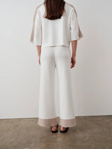 Rear view of a woman wearing a white and beige contrast collar knit polo top with matching trousers, emphasizing the cropped, boxy silhouette.