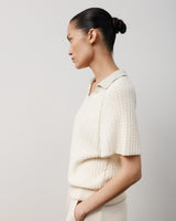 Profile view of a woman wearing a white textured knit polo top with a relaxed fit and V-open neckline.