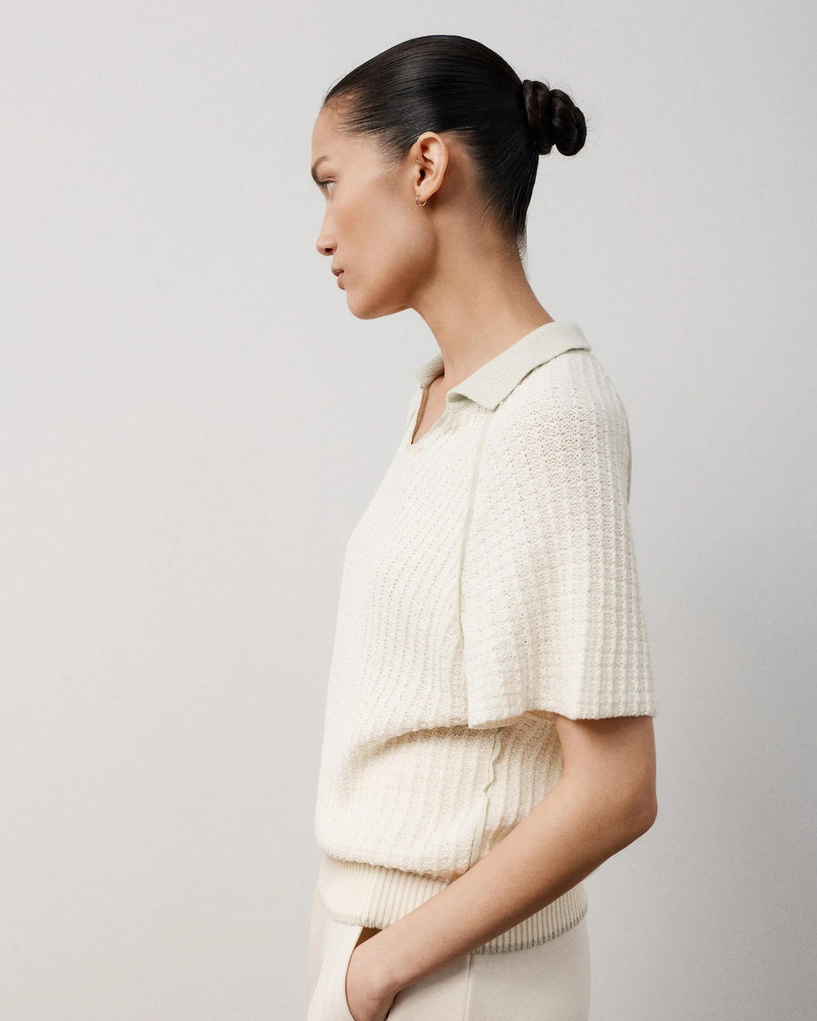 Profile view of a woman wearing a white textured knit polo top with a relaxed fit and V-open neckline.