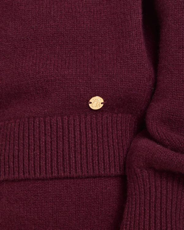 Detail of Kasima Cashmere Blend Knit Sweater in rich fig with gold-finish branded disc.