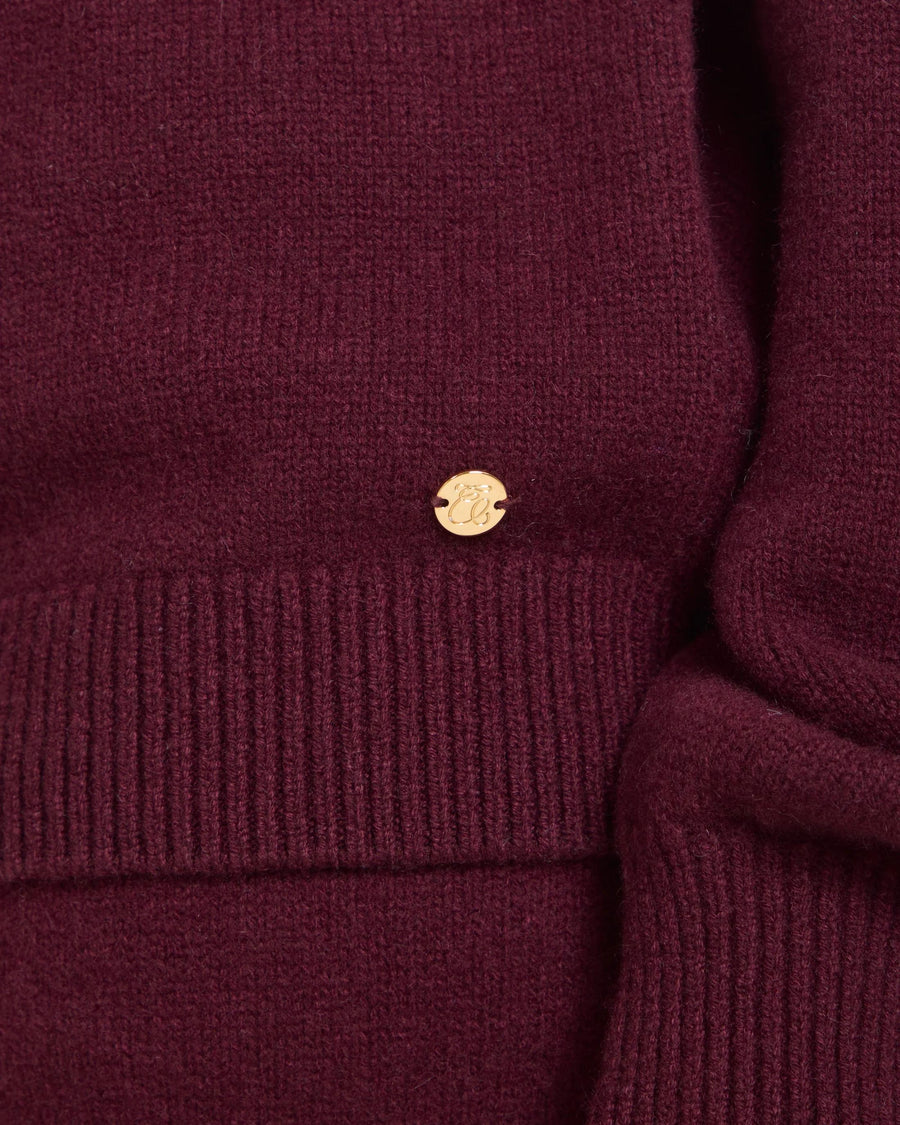 Detail of Kasima Cashmere Blend Knit Sweater in rich fig with gold-finish branded disc.