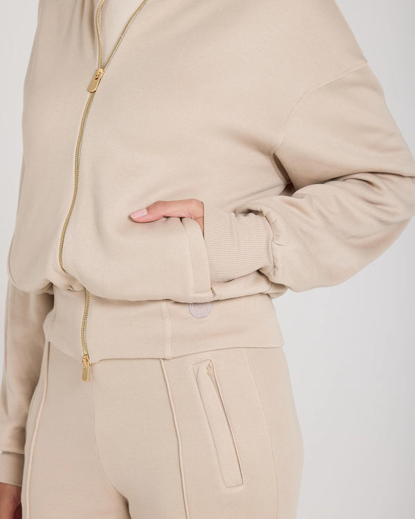 Side view of the Mello Lyocell Fleece Zip-Through Jacket in beige, showcasing gold-finish zip and embroidered pocket.