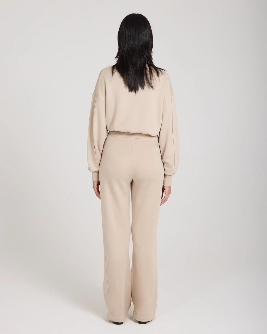 Back view of model wearing beige wide-leg lyocell fleece pants by Emello, showcasing relaxed fit and subtle elegance.