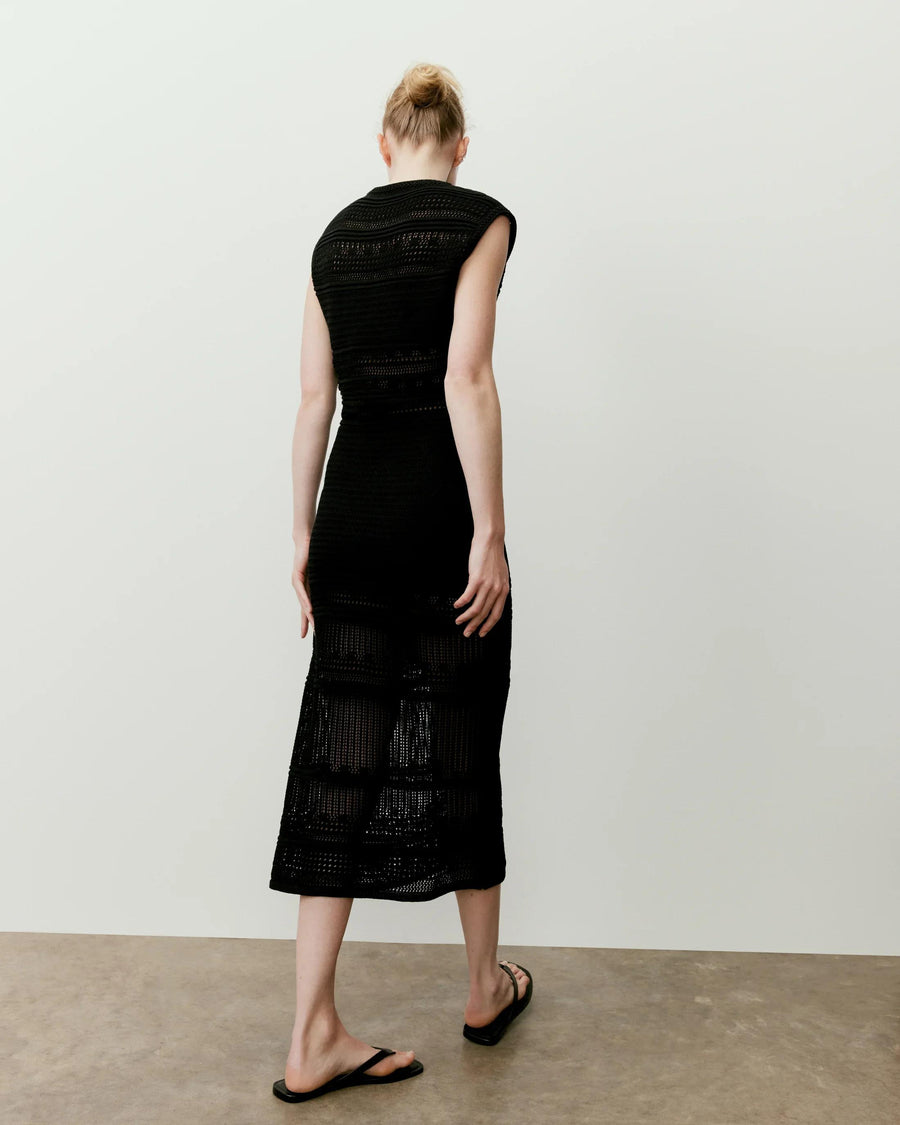 Back view of a model in a black panelled open knit midi dress showcasing its structured yet breathable design.