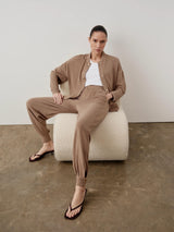Woman wearing the Modal Popper Jacket and matching trousers, seated on a plush white bench, embodying a relaxed yet sophisticated style.