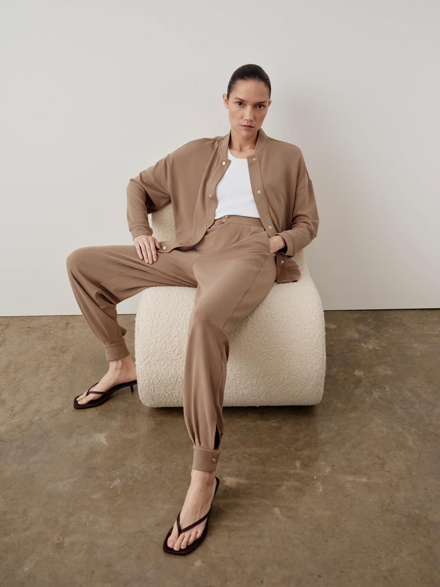 Woman wearing the Modal Popper Jacket and matching trousers, seated on a plush white bench, embodying a relaxed yet sophisticated style.