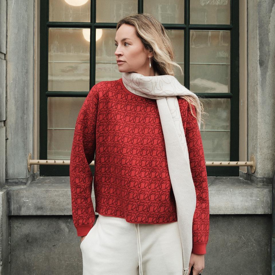 Woman wearing red Emello monogram knit and ivory scarf outside classic building