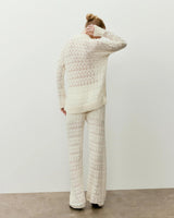 Back view of a woman wearing a cream open knit polo top, showcasing its elegant open-stitch design.