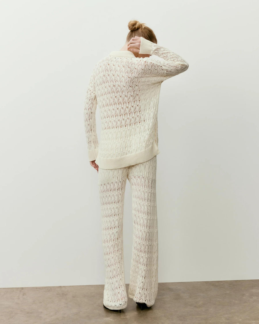 Back view of a woman wearing a cream open knit polo top, showcasing its elegant open-stitch design.