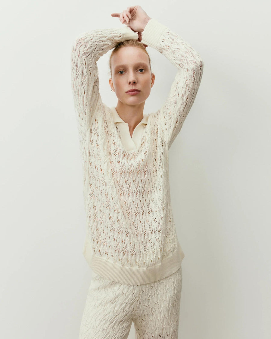 Cream open knit cotton polo top with ribbed collar, elegantly worn in a poised stance.