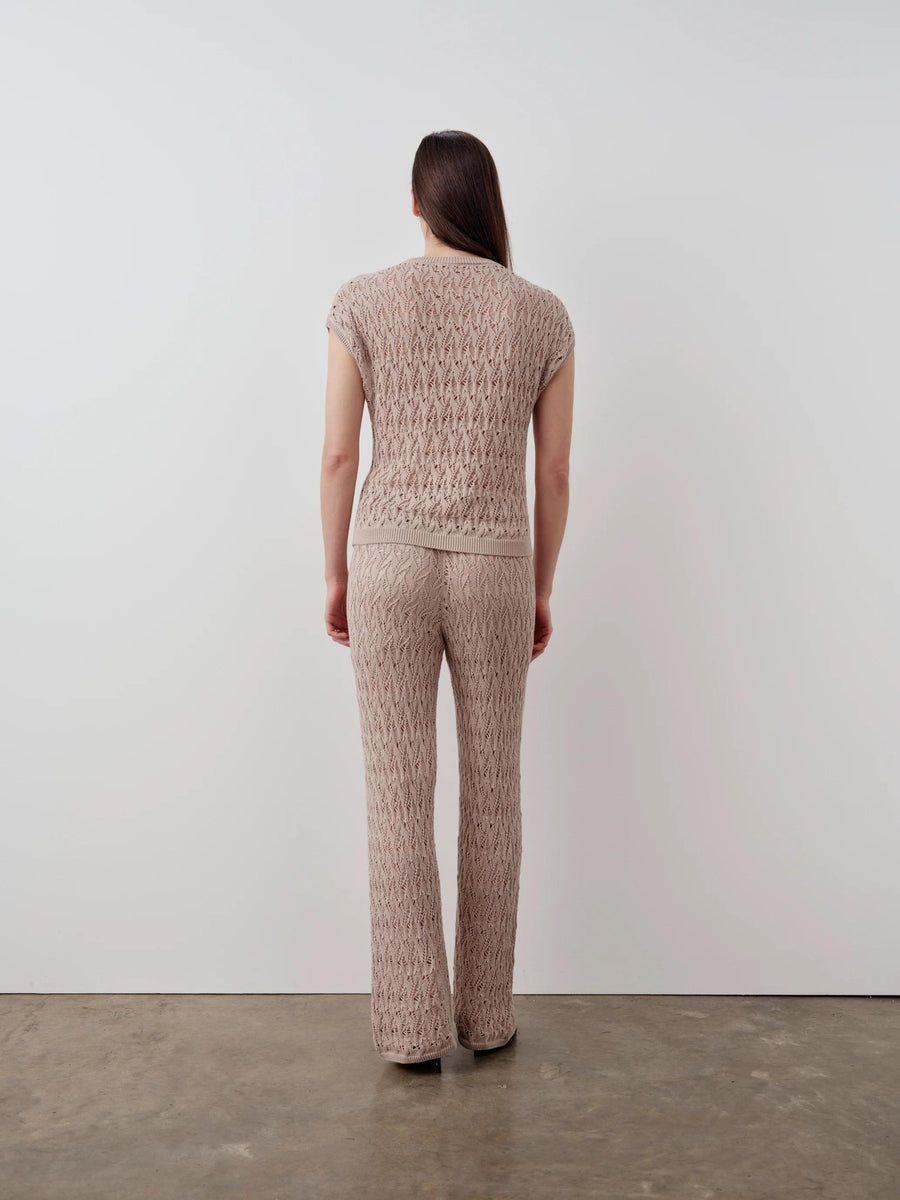 Rear view of a model wearing the Emello Open Knit Short Sleeve Top in neutral beige, showcasing the intricate open-stitch pattern.