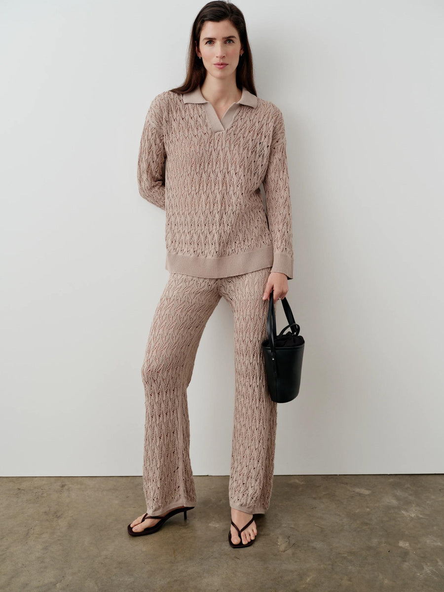 An elegant woman dressed in a neutral open-knit polo top and matching pants, showcasing Emello's refined luxury womenswear.