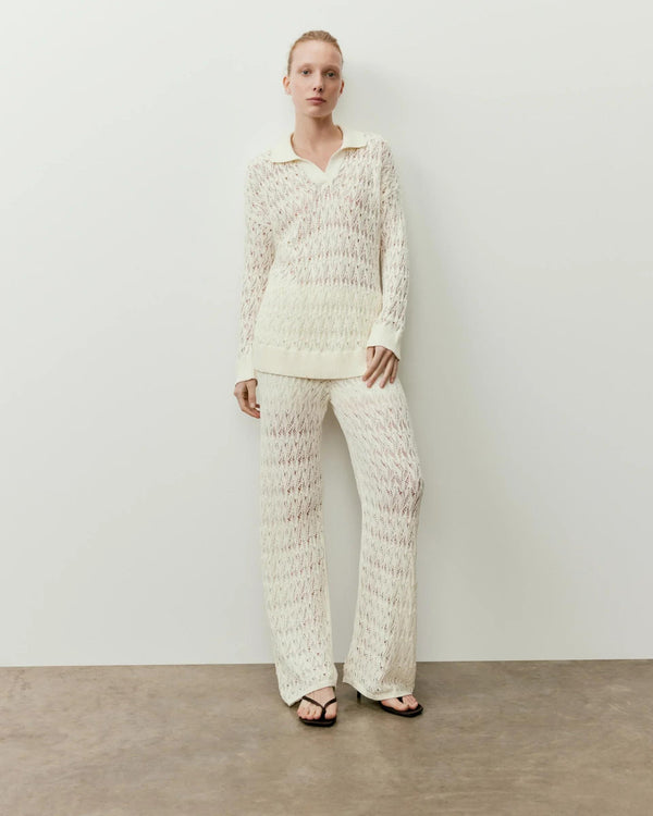 Model wearing Emello's open knit trousers in cream, designed with Italian-spun cotton and a relaxed straight-leg fit.