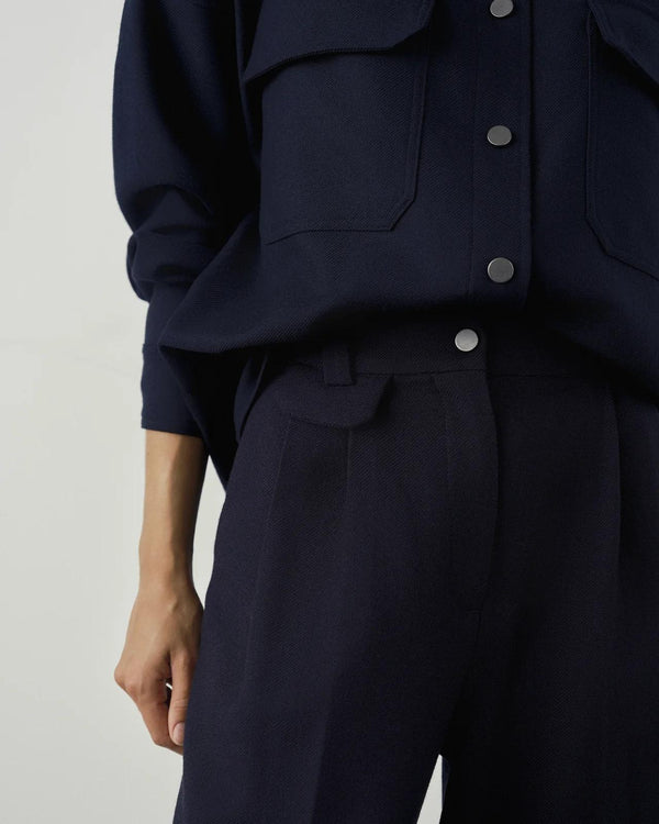 Pleated wool twill trousers in deep navy with front pleats and brushed-metal fastening, styled with coordinating overshirt.